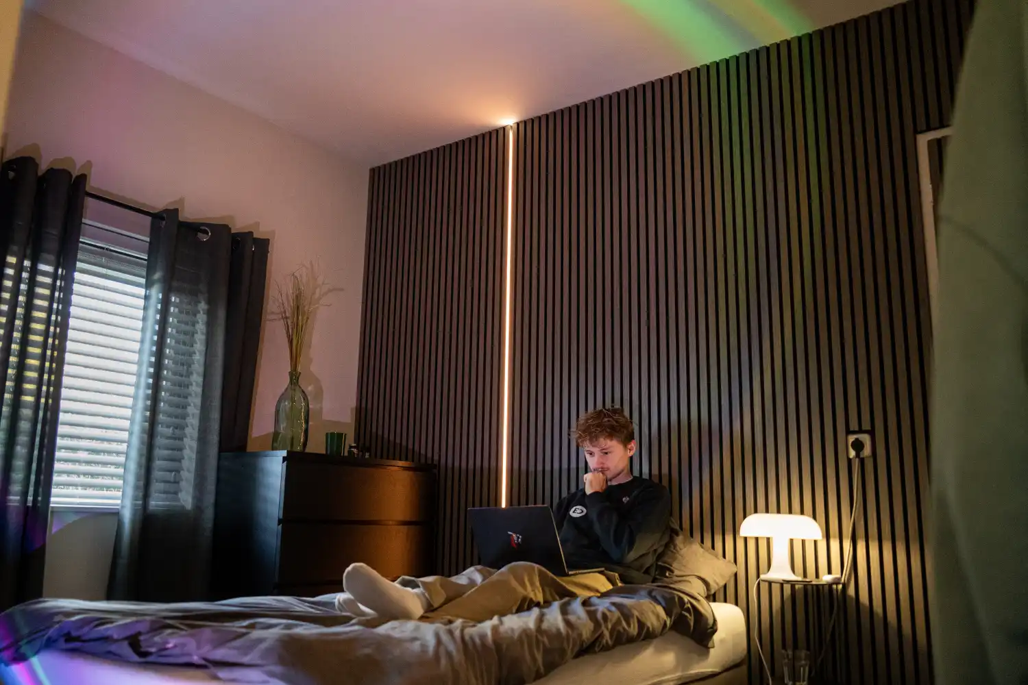 Man werkt op laptop in slaapkamer met warme LED-strip verlichting langs de muur